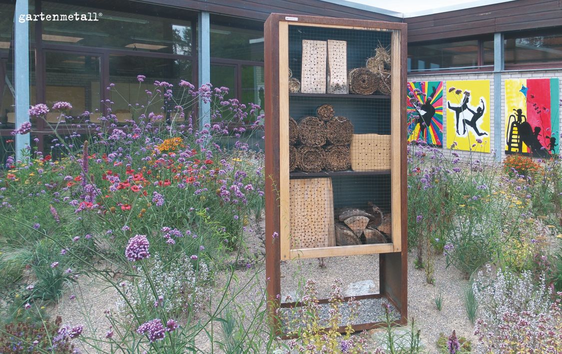 Insektenhotel mit Rahmen aus Cortenstahl im Kräutersand