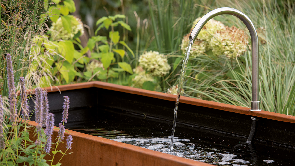 Gebogenes Brunneneinlaufrohr RAURIS am Beckenrand eines Wassertrog AQUA LINEA aus Cortenstahl