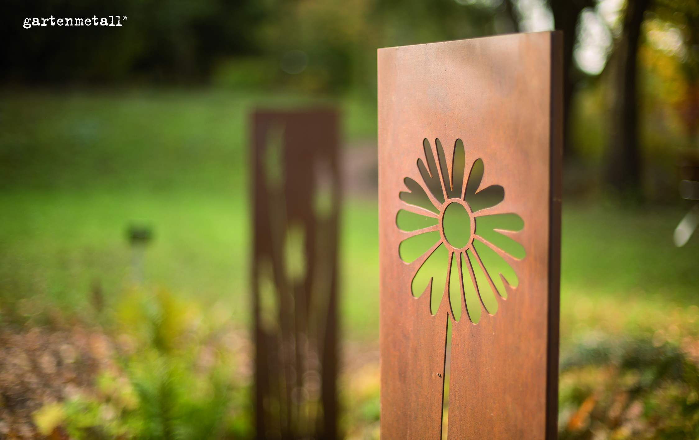 Metallplatte mit Blumenmotiv ausgeschnitten, steht still vor unscharfem grünen Hintergrund. Links oben der Text: 'gartenmetall®'.