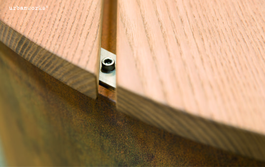 Holzpaneel bewegt sich auf Metallstruktur, umgeben von rostiger, brauner Oberfläche. Text im Bild: „urbanworks“.