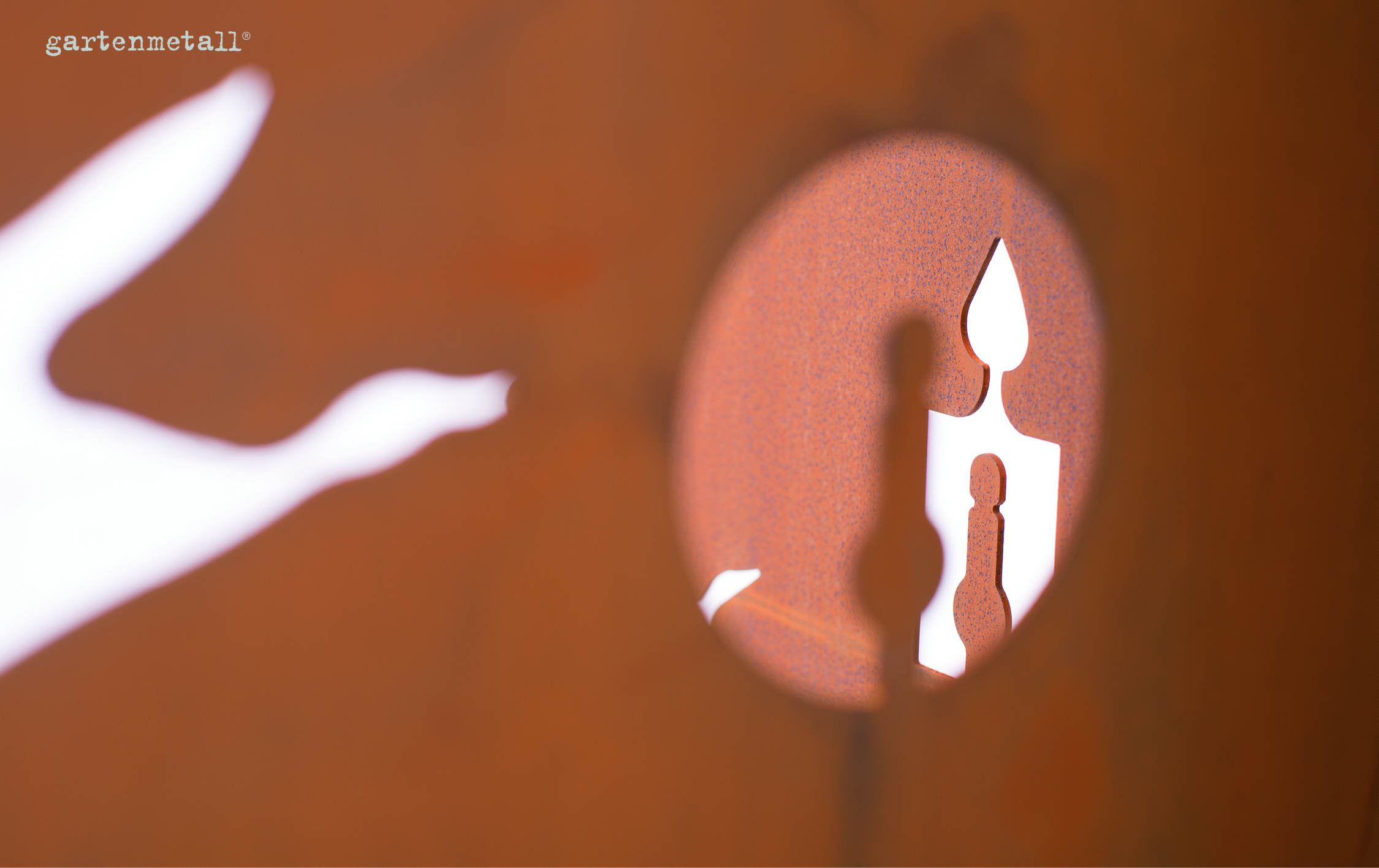 Eine runde Metallplatte mit ausgestanzten Formen, zeigt Silhouetten. Im Hintergrund ein verschwommener, orangefarbener Bereich. Text: 'gartenmetall®'.