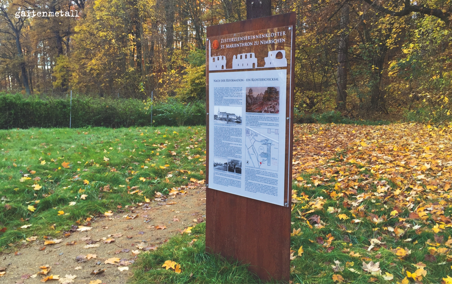 Schild beschreibt Geschichte des Zisterzienserinnenklosters St. Marienthron zu Nimbschen, im herbstlichen Wald. Text: 'Nach der Reformation - Ein Klosterschicksal.' Umgebung mit fallenden Blättern.