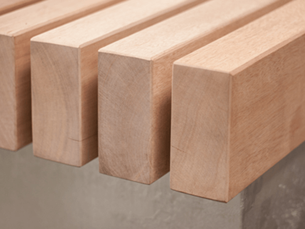 Holzbretter liegen parallel nebeneinander, ruhen auf einer Metallstruktur, umgeben von einem neutralen, minimalistischen Hintergrund aus Beton, ohne sichtbare Verzierungen oder Text.