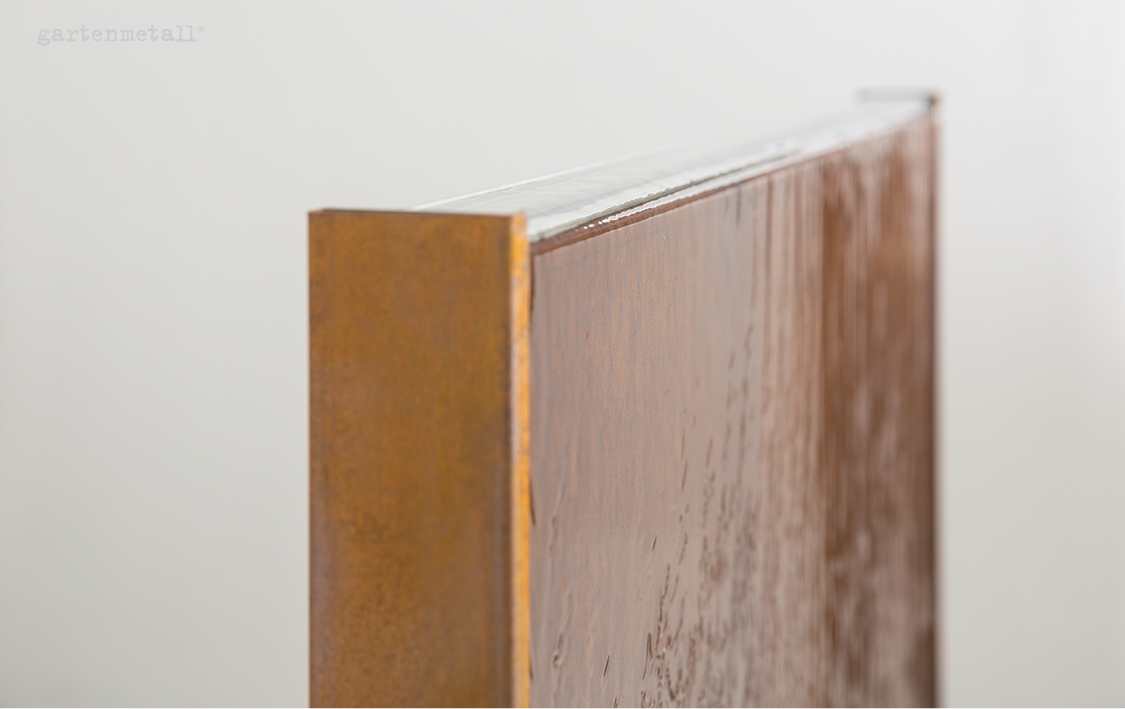 Ein rechteckiges Metallobjekt mit rostbrauner Oberfläche, steht vertikal, links im Fokus, im Hintergrund helle, unscharfe Wand. Text oben links: „gartenmetall®“.