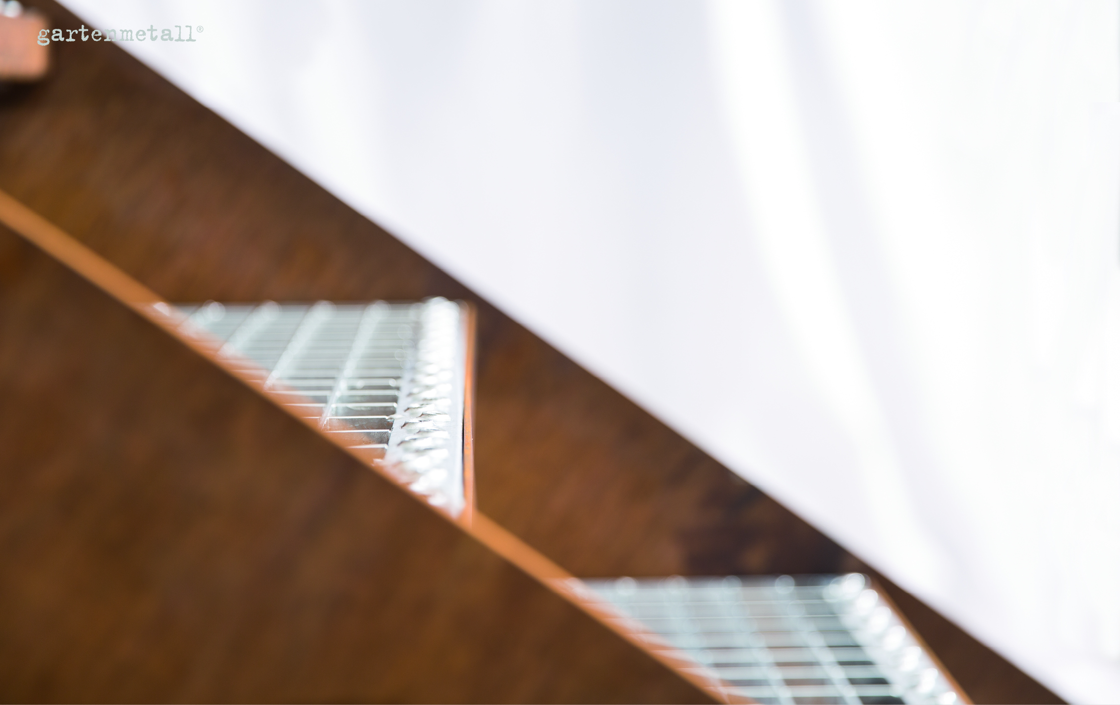 Metallstufen reflektieren Licht, schräg angeordnet vor unscharfem Hintergrund. Im Bildtext oben links steht 'gartenmetall®'.