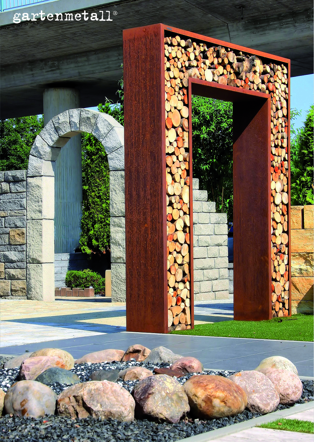 Holzgefüllter Metallrahmen, stehend vor Steinbögen, in einem architektonischen, gartenähnlichen Bereich mit dekorativen Steinen. Text: 'gartenmetall®'.