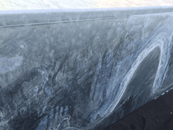 Eine graue Mauer zeigt Schmutzspuren und eine helle, gebogene Linie, umgeben von einer dunklen, teerähnlichen Oberfläche im Hintergrund.