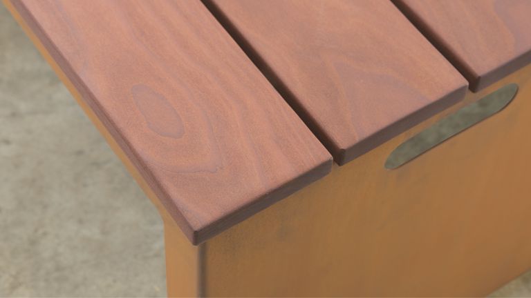 Holzbank mit glatter, brauner Oberfläche und zwei getrennten Planken, steht auf einem Betonboden. Eine Aussparung seitlich dient als Tragegriff.