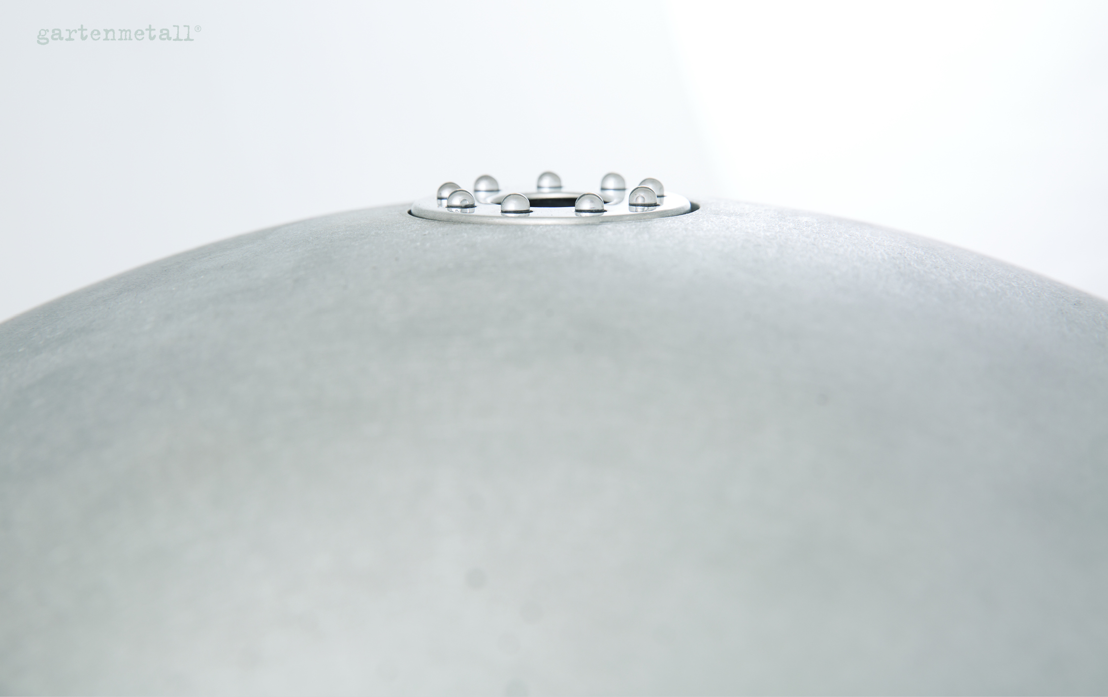 Kuppelförmiges Objekt hält Wassertropfen, auf metallischer Oberfläche platziert, minimalistische, helle Umgebung. Text: 'gartenmetall®'.