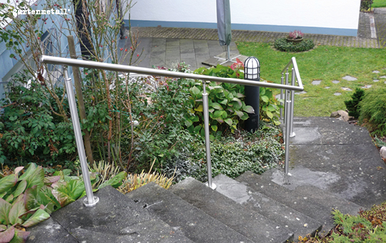 Ein Edelstahlgeländer verläuft entlang einer steinernen Treppe, die durch einen Garten mit grünen Pflanzen und einem beleuchteten Weglampen führt. Text: 'gartentexte' links oben.