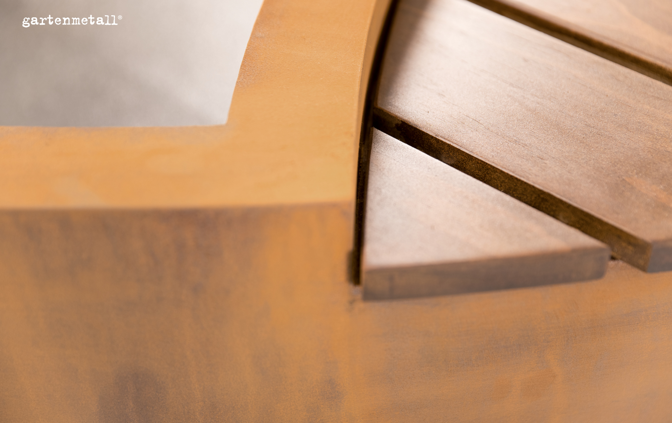 Ein Holzkanten-Detail liegt unbewegt in Nahaufnahme auf einer hellen, unscharfen Oberfläche, links oben steht der Text 'gartenmetall®'.