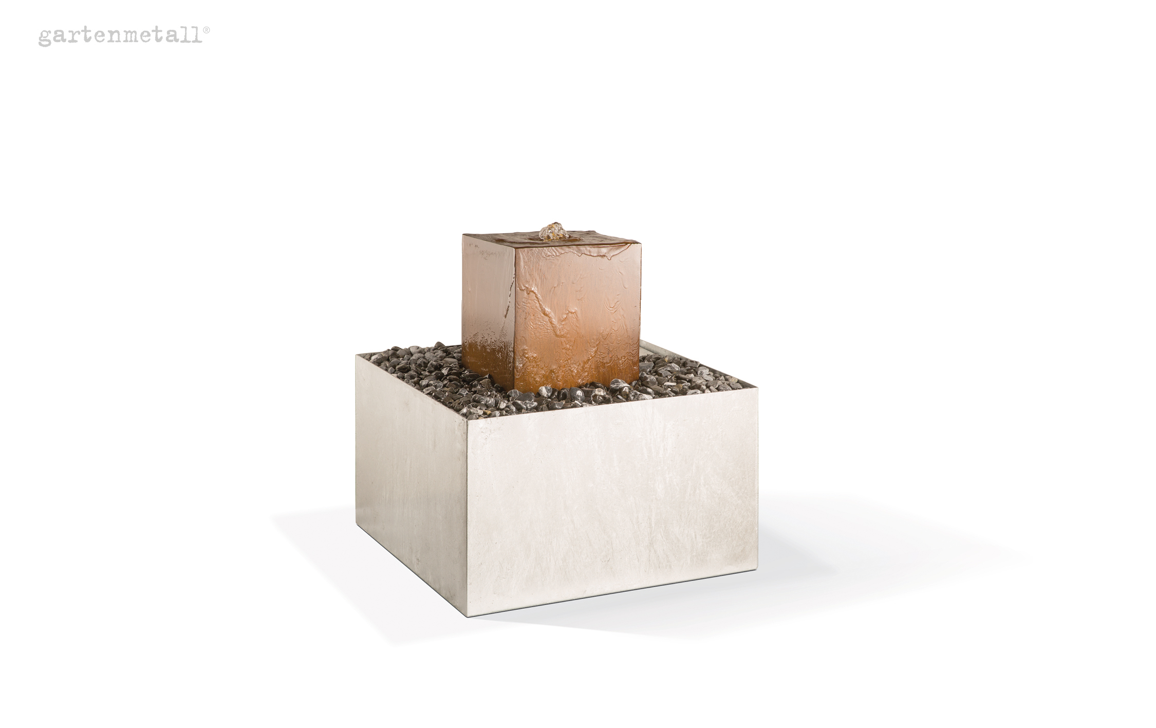 Wasserquelle entspringt aus bronzefarbener Metallwürfel-Skulptur, plätschert sanft herunter, umgeben von Kieselsteinen in quadratischem Pflanzengefäß, minimalistische Gartenkunst. Text: 'gartenmetall®'.