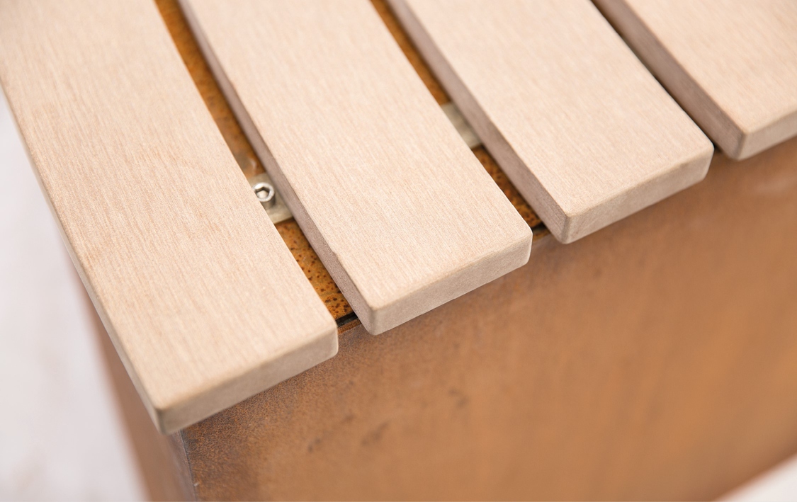 Holzlatten, horizontal angeordnet, befestigt auf einer rostfarbenen Metallunterlage, leicht geneigt fotografiert, wahrscheinlich Teil einer Bank oder eines Möbelstücks. Umgebung unklar.