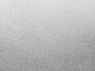 Es handelt sich um eine monochrome Fläche mit feiner, grafitartiger Struktur, die gleichmäßig das Bild bedeckt und dadurch eine minimalistische, texturierte Erscheinung in einem neutralen Umfeld erzeugt.