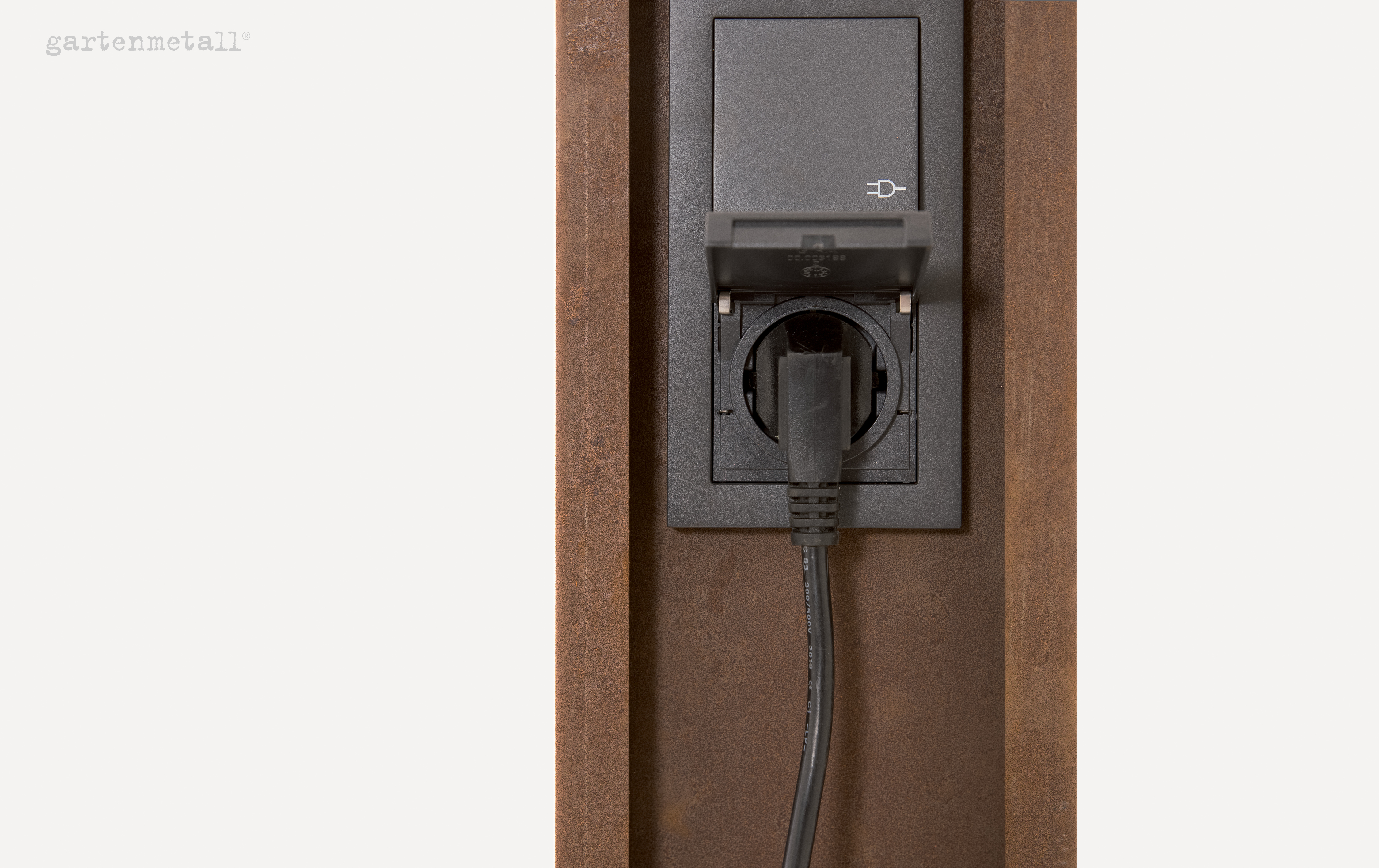 Eine schwarze Steckdose ist mit einem eingesteckten Kabel verbunden, eingebaut in eine rostbraune Metallwand. Links oben steht 'gartenmetall®'.
