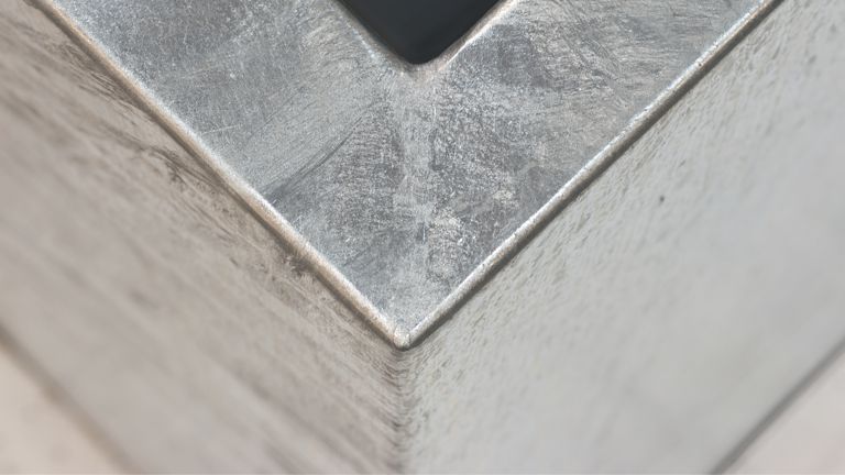 Ecke eines metallischen Rahmens, verläuft schräg in die Tiefe, umgeben von glatten, hellgrauen Flächen.