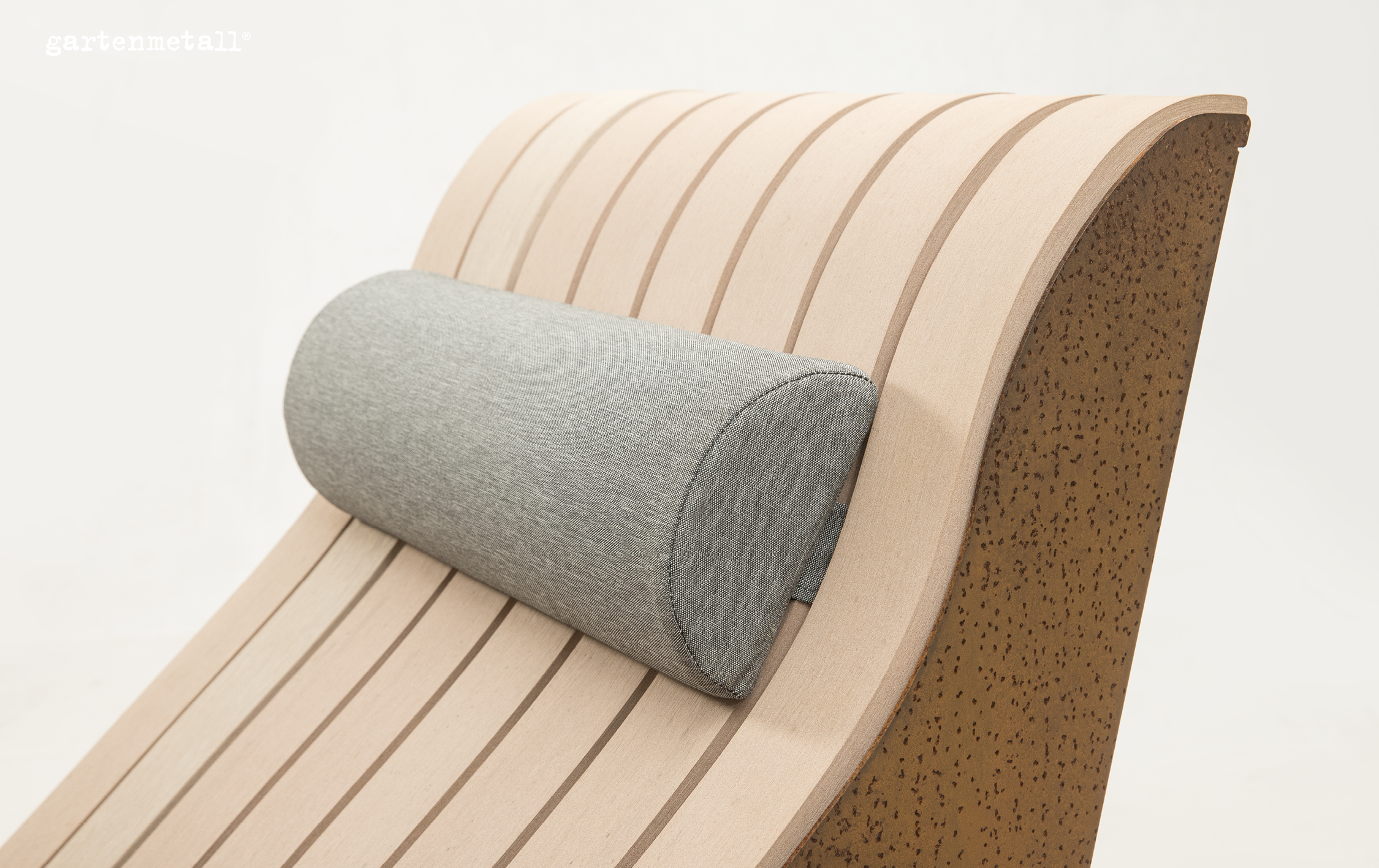 Eine hölzerne Liege mit gepolsterter Rolle stützt den Kopf. Sie steht in einem minimalistisch gestalten Raum. Text: 'gartenmetall®'.