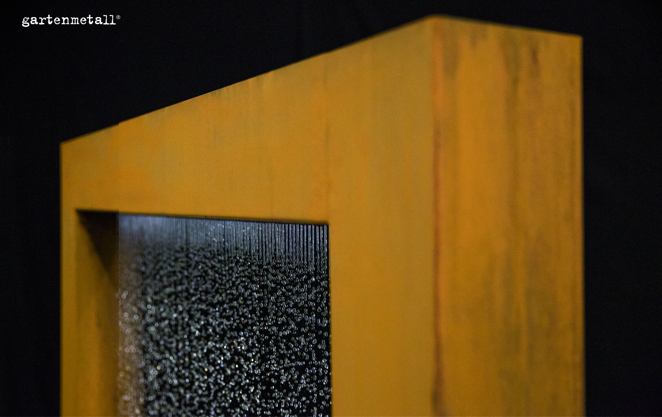 Eine rustikal anmutende Metallskulptur zeigt fließendes Wasser entlang einer strukturierten Fläche. Die Szenerie ist in dunkler Umgebung. Text: 'gartenmetall®'.