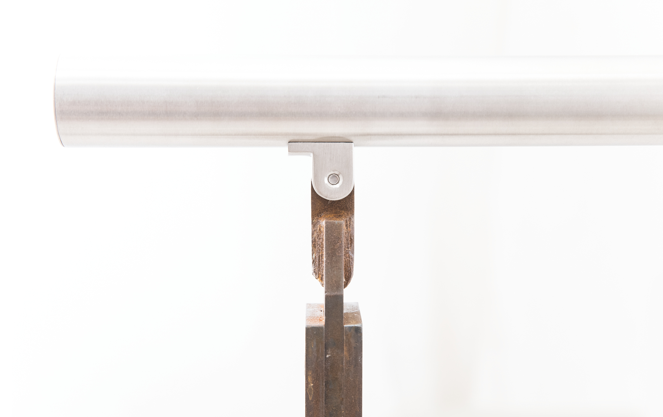 Metallzylinder ruht auf einer metallischen Halterung, verbunden durch eine Schraube, auf einem hölzernen Grundgestell. Minimalistischer Hintergrund lässt das Objekt klar hervortreten.