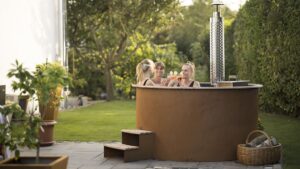 Runder brauner Whirlpool mit zwei Personen, Einstiegstreppe und Ofen auf einer Terrasse im grünen Garten