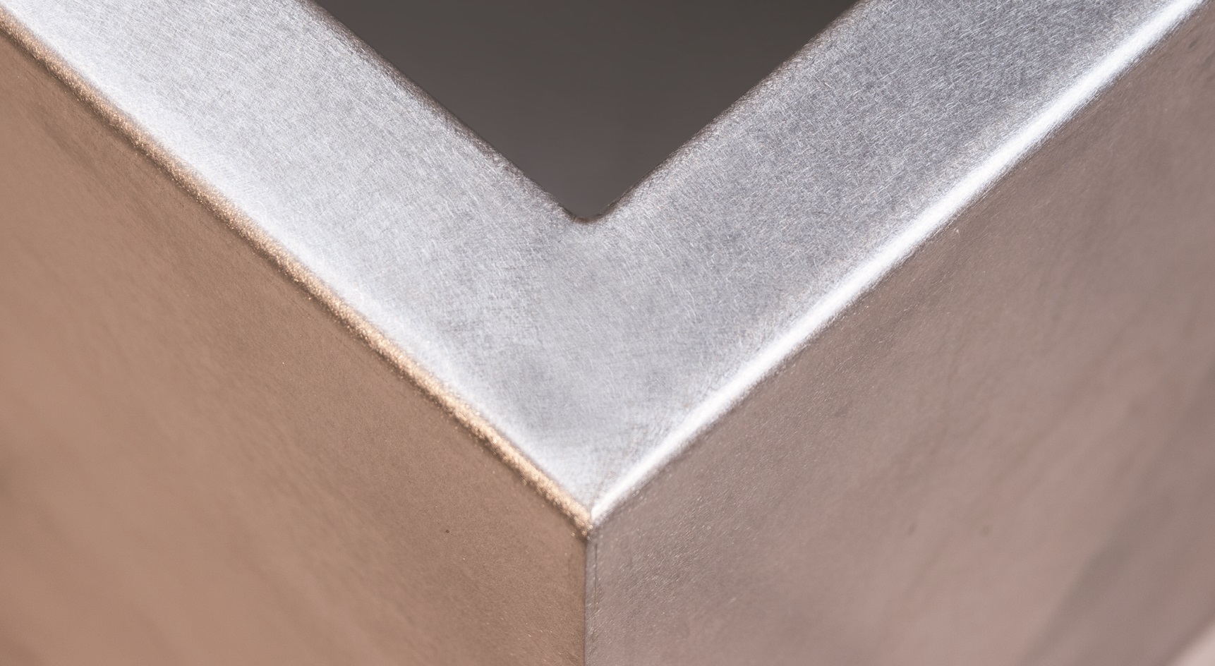 Metallecke reflektiert Licht, befindet sich in ruhigem, neutralem Raum.