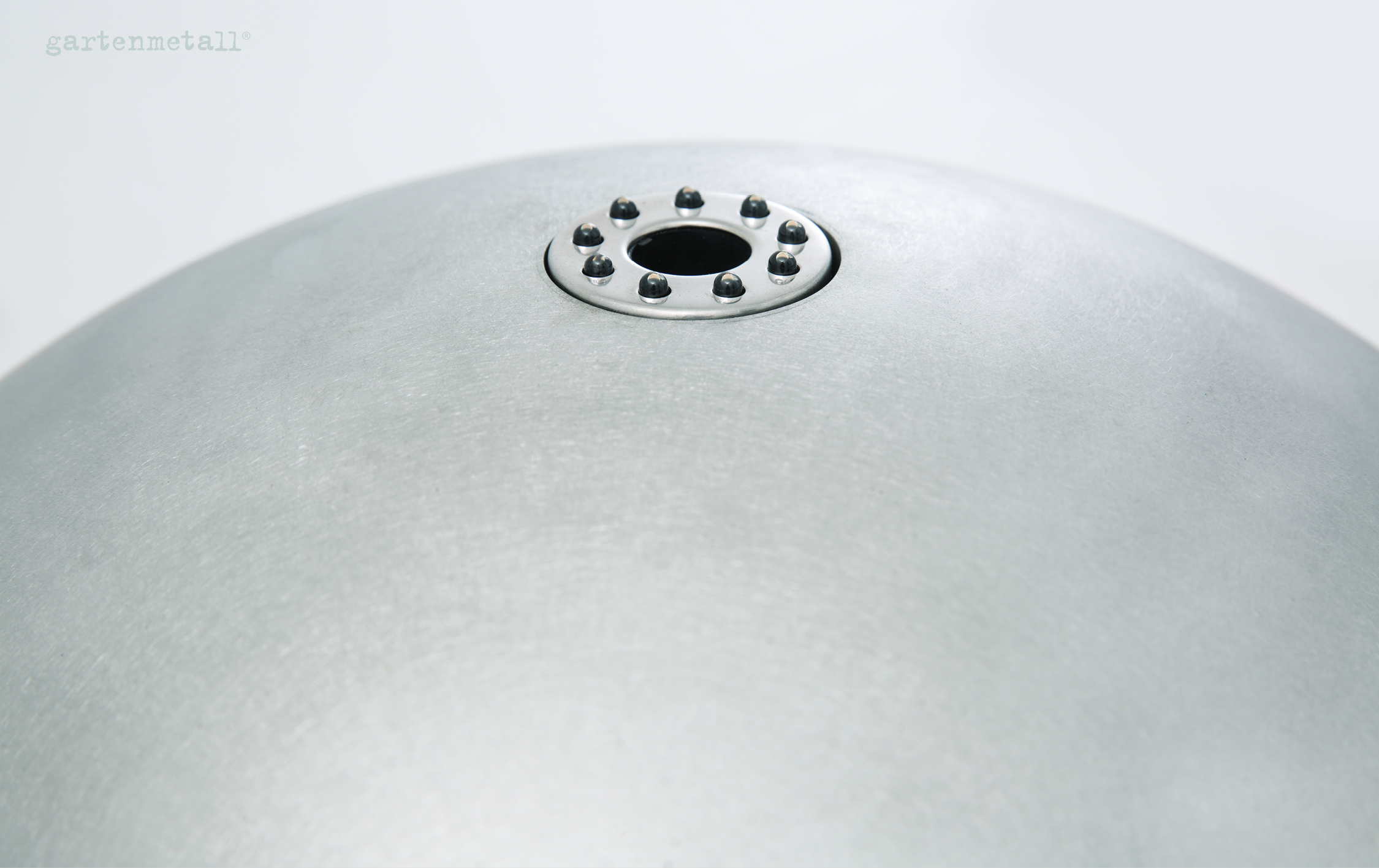 Metallkugel mit zentrischem Loch, umgeben von kleinen Nieten, liegt auf weißem Hintergrund, links oben steht „gartenmetall®“.
