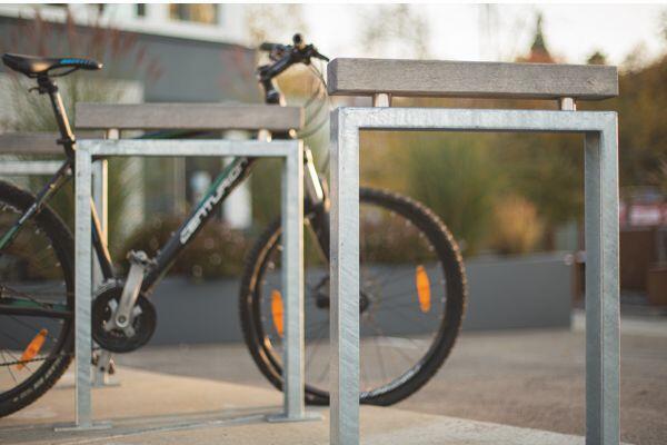 Ein Fahrrad steht an einem modernen Metall-Fahrradständer im Freien, umgeben von unscharfer Vegetation und Gebäuden im Hintergrund. Das Fahrrad trägt den Schriftzug 'CMTB 2000'.