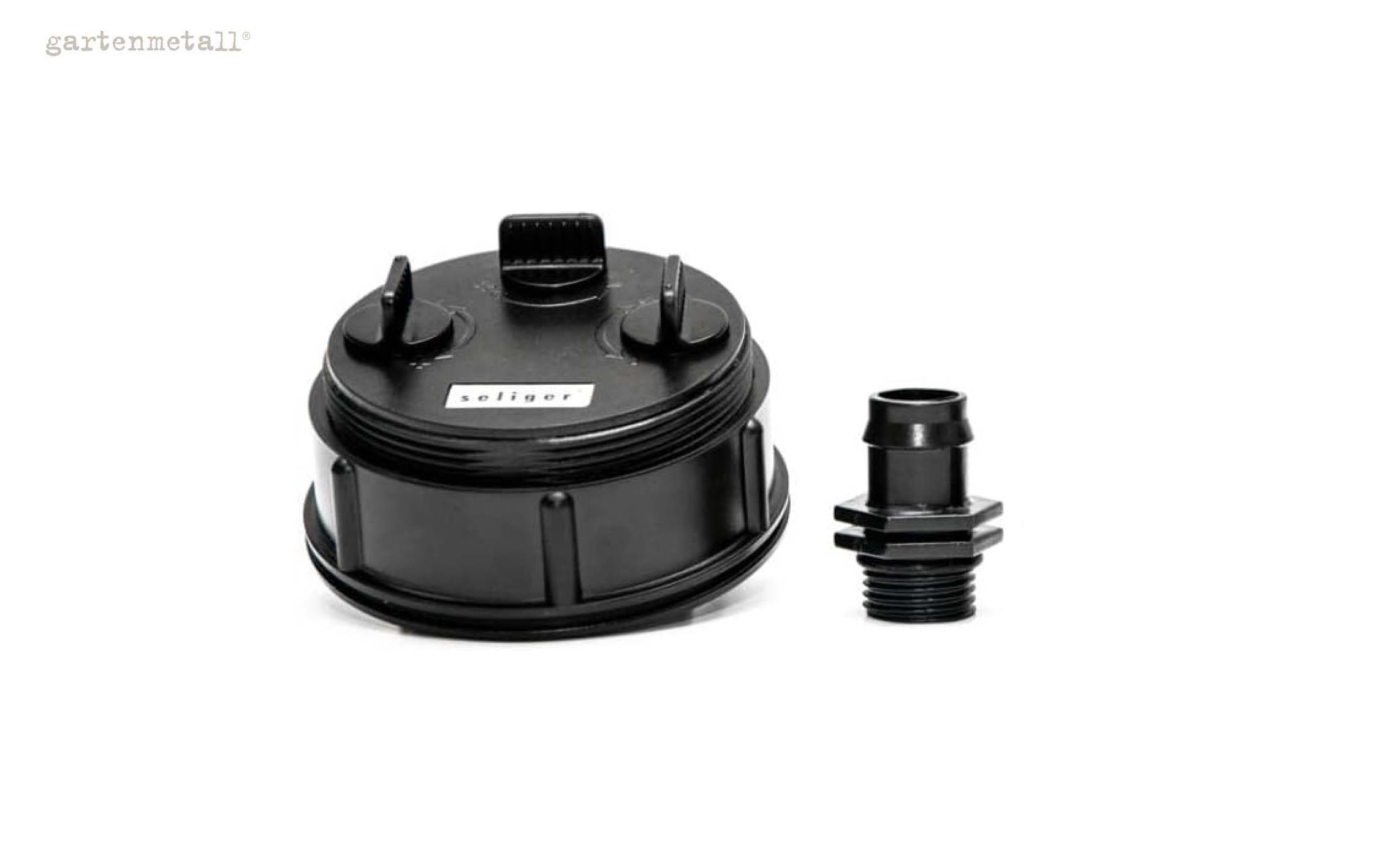Schwarzer Plastikdeckel mit zwei Drehgriffen liegt neben einem Anschlussstück. Der Deckel trägt die Aufschrift 'seliger' und oben links im Bild steht 'gartenmetall'. Hintergrund ist weiß.