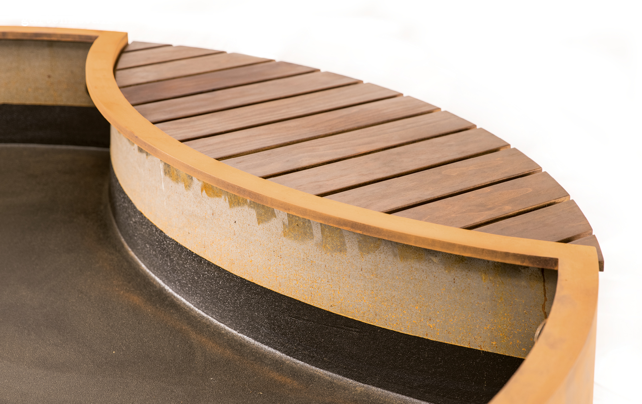 Runder Grill aus Metall mit hölzerner Abdeckung, steht auf einer schwarzen Fläche, von rostiger Patina umgeben, in minimalistischem, modernem Design.