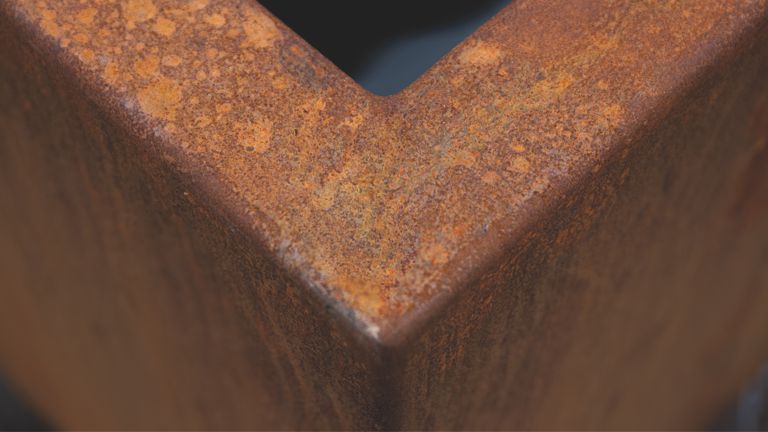 Rostige Metallkante mit eckiger Form, zeigt deutliche Verfärbungen und Oxidationsspuren, steht vor einem dunklen, unscharfen Hintergrund.