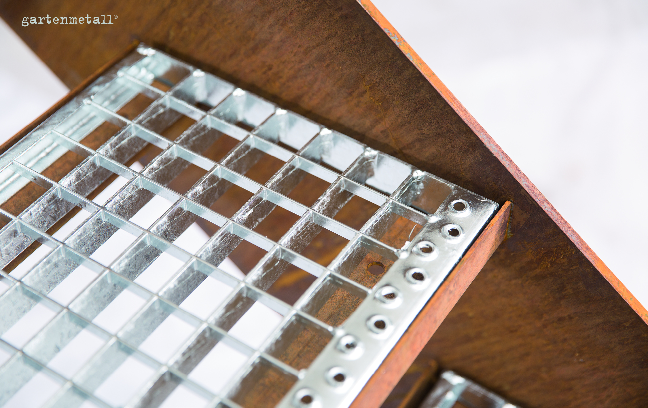 Metallgitter liegt auf rostigem Metallwinkel, fest verschraubt, darüber Text 'gartenmetall®', helle, unscharfe Umgebung.