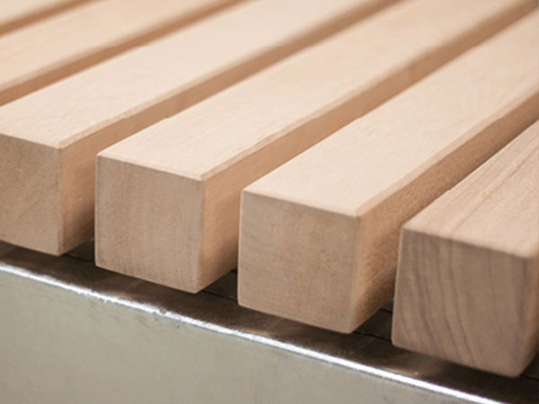 Holzbalken liegen parallel auf einer silbernen Metalloberfläche, geordnet in gleichmäßigen Abständen, in einem gut beleuchteten Raum.